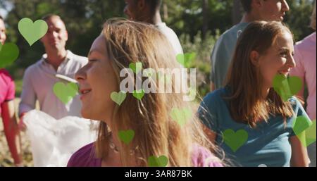 Image de cœurs verts sur divers groupes heureux ramassant des ordures dans la campagne Banque D'Images