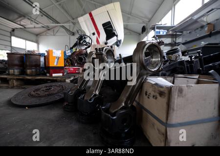 Les pistons avec bielles sont disposés sur le plancher d'un atelier de réparation ou d'un entrepôt, entourés par d'autres composants et outils de moteur. Banque D'Images