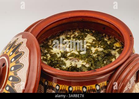 Un pot traditionnel en argile révèle un délicieux plat vert à base d'herbes fraîches et d'ingrédients crémeux, mettant en valeur les traditions et les saveurs culinaires locales. Banque D'Images