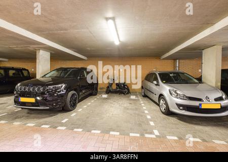 Un parking couvert avec un SUV noir, une voiture argentée et un scooter. L'environnement met en évidence des espaces de stationnement organisés avec des lignes claires. Banque D'Images