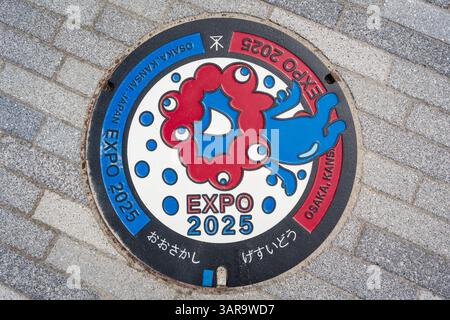 Osaka, Japon - 16 avril 2025 : Manhole cover avec une image colorée de MYAKU-MYAKU, la mascotte officielle de l'Expo 2025 d'Osaka. Banque D'Images