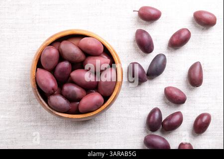 Olives Kalamata avec fosse, dans un bol en bois sur lin. Grandes olives violettes cueillies à la main, à la texture lisse et charnue, nommées d'après la ville grecque Kalamata. Banque D'Images