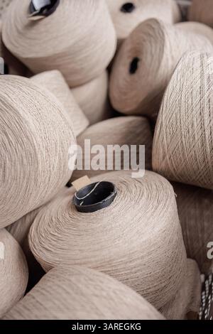 Gros plan de plusieurs cônes de fil beige empilés pour la fabrication de textiles dans une installation de production de tissus ou de tricots. Banque D'Images