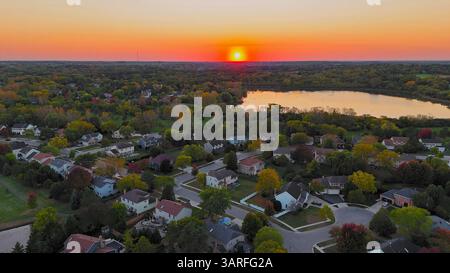 Coucher de soleil sur le paysage de banlieue de Chicago. Une vue aérienne captivante d'une banlieue de Chicago au coucher du soleil avec un soleil orange éclatant qui s'enfonce dans l'horizon. Banque D'Images