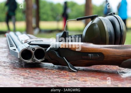 Un fusil de chasse sportif à double canon et des écouteurs pour le tir reposent sur une table en bois sur le fond du champ de tir Banque D'Images