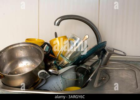 La vaisselle sale et non lavée est empilée dans l'évier de la cuisine. Tasses, assiettes, pots, fourchettes et cuillères non lavés. Une montagne de plats désordonnés et usagés Banque D'Images