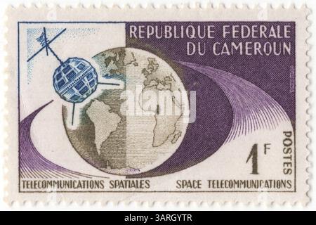 CAMEROUN - 9 février 1963 : timbre-poste bleu foncé, olive et violet à 1 franc CFA représentant Telstar et Globe. La première liaison télévisuelle entre les États-Unis et l'Europe via le satellite de communication Telstar lancé par la NASA. Ce satellite a également transmis des données informatiques entre deux ordinateurs IBM 1401. Un test effectué le 25 octobre 1962 a envoyé un message d'Endicott, New York, à une station terrienne à Andover, Maine. Le message a été transmis via le satellite Telstar à une station terrienne en France, où il a été décodé par un deuxième IBM 1401 à la Gaude, en France Banque D'Images