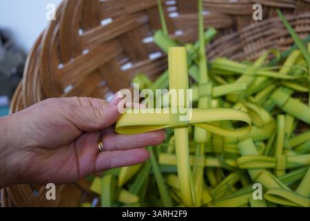 Coutume de Pâques : la main de la femme tient une croix faite à la main qui a été faite à partir de feuille de palmier - plus de croix sont dans un panier tissé qui vont être partagés Banque D'Images