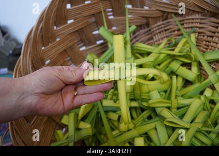 Coutume de Pâques : la main de la femme tient une croix faite à la main qui a été faite à partir de feuille de palmier - plus de croix sont dans un panier tissé qui vont être partagés Banque D'Images