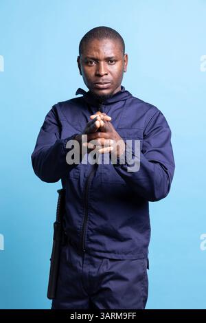 Portrait du personnel de sécurité afro-américain imitant la tenue d'un pistolet imaginaire, tir à la cible avec ses mains en forme d'arme à feu. Agent de garde masculin agissant sérieusement en studio. Banque D'Images