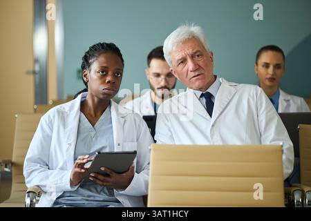 Groupe de professionnels de la santé, dont une personne âgée, discutant de la stratégie de traitement. Jeunes médecins masculins et féminins concentrés sur les tablettes numériques Banque D'Images