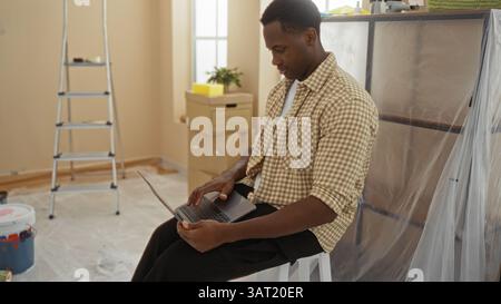 Jeune homme utilisant un ordinateur portable dans le salon récemment rénové avec échelle et boîtes montrant la rénovation en cours et un cadre intérieur suggérant un St frais Banque D'Images