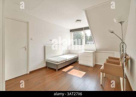 Cette chambre moderne lumineuse et aérée présente un design minimaliste avec du parquet, un mobilier simple et une lumière naturelle abondante. Banque D'Images