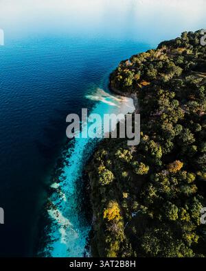 Île tropicale luxuriante avec une forêt dense rencontrant une plage de sable blanc et des eaux turquoises, capturées d'en haut en Thaïlande. Banque D'Images
