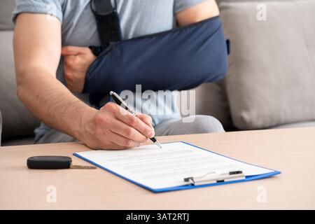 Gros plan d'un homme mains avec bras cassé signant un document d'assurance après un accident de voiture à la maison Banque D'Images