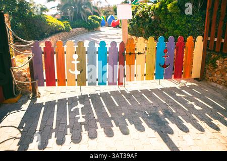 Petite porte en bois coloré faite de planches verticales peintes dans différentes couleurs vives, certaines comportant des découpes d'ancre. La lumière du soleil jette long, distinct Banque D'Images