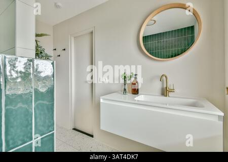Une salle de bains élégante avec carrelage vert, un miroir circulaire et un lavabo mural blanc, créant une ambiance élégante et contemporaine. Banque D'Images