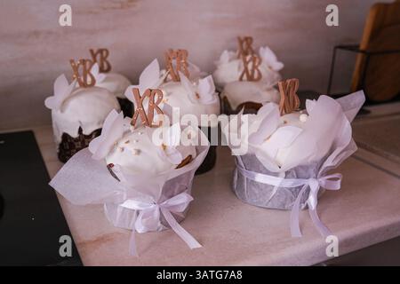 Moscou, Russie, 18.04.25. Une rangée de cupcakes blancs avec XB et XB dessus. Les cupcakes sont décorés de glaçage blanc et ont un noeud sur le dessus Banque D'Images