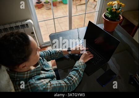 Une femme travaillant sur son ordinateur portable à un bureau dans un bureau à domicile confortable, avec une lumière naturelle chaude et une ambiance sereine, créant un confortable et producti Banque D'Images