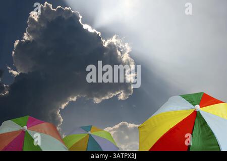 Parapluies ou parasols colorés devant un nuage de pluie sombre - parapluies arc-en-ciel sous nuages de tempête Banque D'Images