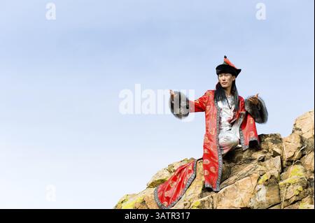 Jeune homme asiatique en costume mongol fin est assis sur le rocher Banque D'Images