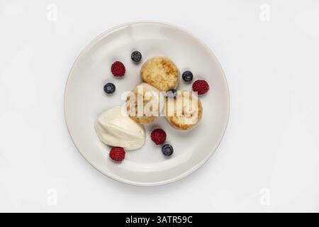Gâteaux au fromage et différentes baies sur une assiette sur un fond isolé de studio Banque D'Images