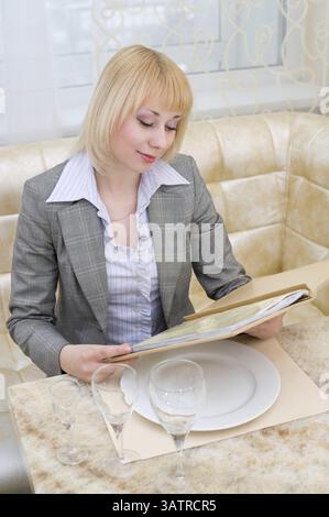 Jeune femme blonde lisant le menu au restaurant de première classe Banque D'Images