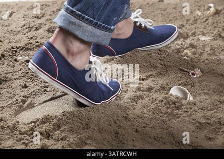Jambes de l'homme et empreinte sur le sable Banque D'Images