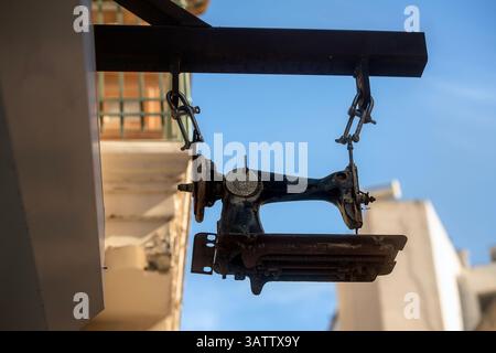 Ancienne machine à coudre vintage accrochée à un cadre métallique à l’entrée d’un tailleur comme signe original et créatif. Banque D'Images