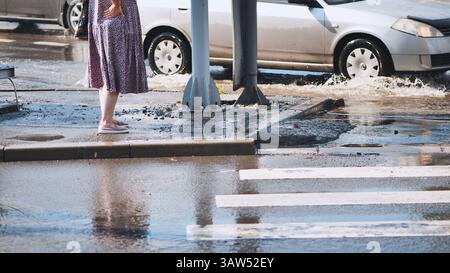 Femme attendant sur le trottoir à côté du passage inondé, éclaboussée en passant le véhicule à travers une profonde flaque Banque D'Images