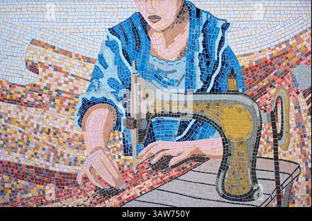 Détail d'une mosaïque sur un mur représentant une femme utilisant une machine à coudre. ? ?'Mosaico di Rosa Genoni' une œuvre d'art dynamique inaugurée en mars 2024 à Milan. Cette mosaïque polychrome rend hommage à Rosa Genoni (1867-1954), couturière italienne pionnière, créatrice de mode et militante pour l'émancipation et la paix des femmes. Genoni a joué un rôle déterminant dans l'éloignement de la mode italienne des influences françaises, défendant les designs et l'artisanat indigènes.  ? Conçue par les artistes Sonia D'Errico et Cristian Colucci, la mosaïque comprend plus de 16000 carreaux de céramique Piazzetta Lilla Brignone/ via Porlezza, Milan, Italie Banque D'Images