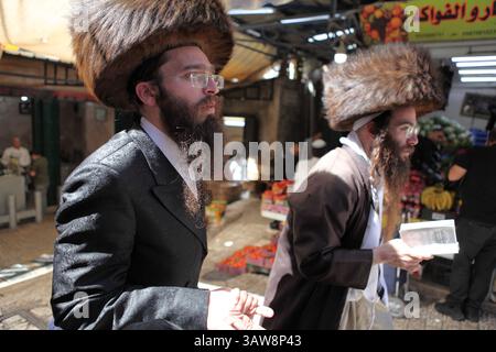 Les hommes juifs ultra orthodoxes se précipitent dans une rue du marché de la vieille ville, tous deux portent un chapeau de fourrure ou un shtreimel, on peut lire dans un livre de prières. Vieille Jérusalem. Banque D'Images