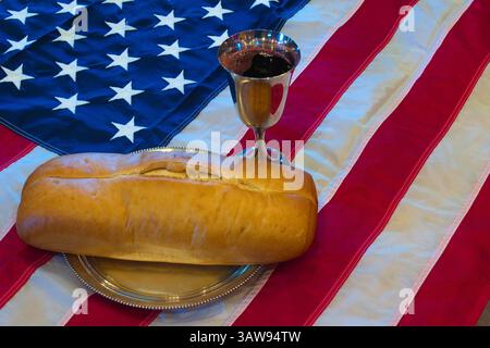 Un calice de communion avec du vin et une miche de pain se trouvent au-dessus d'un drapeau américain, symbolisant le nationalisme chrétien. Banque D'Images