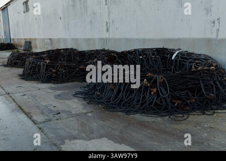 De vieux filets de pêche usés sont empilés sur le sol près d'un entrepôt côtier, suggérant des activités de pêche récentes ou le stockage d'équipement Banque D'Images