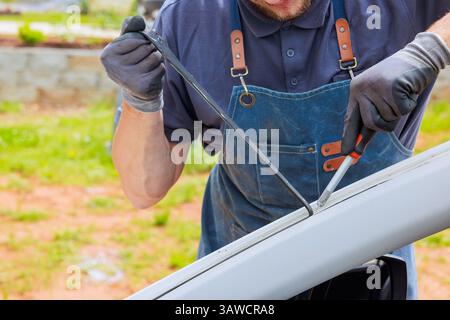 Le travail de mécanicien enlève le mastic silicone endommagé sur la carrosserie de la voiture pendant les remplacements de pare-brise Banque D'Images