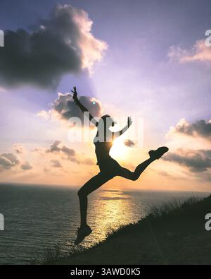 Silhouette de femme sportive en bikini faisant saut de danse devant une belle vue de coucher de soleil sur la mer et le ciel. Mode de vie actif dirung voyager Banque D'Images