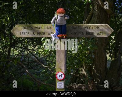 Personne de Yarnbomb attachée à fingerpost (chemin public de longue distance, Ebor Way, lien Dales Way) gros plan - Menston, West Yorkshire, Angleterre Royaume-Uni. Banque D'Images