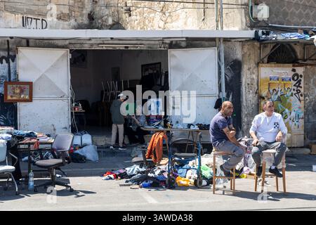 Haïfa, Israël, 16 avril 2025, deux hommes, semblant être du moyen-Orient d'après leurs traits, assis sur des tabourets devant un magasin ou un marché encombré Banque D'Images