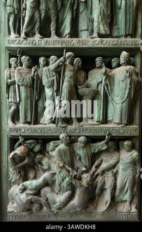 Détail du panneau de bronze de la porte d'entrée gauche au Duomo di Milano représentant des scènes avec des figures en relief et des inscriptions latines. L'inscription supérieure est « THEODOSIVS et VALENTINIANVS VRBEM HONORIFICE INGRESSI », qui se traduit par « Théodose et Valentinien sont entrés honorablement dans la ville ». L'inscription du milieu, 'TEMPIO CLAVSIS POSTIBVS ARCET CRVENIVA CAESAREAM', se traduit par 'avec les portes du temple fermées, il empêche le sanglant César d'entrer'. Les scènes représentent divers personnages, certains en togas ou en tenue militaire, engagés dans ce qui semble être des actes cérémoniels ou narratifs. Milan, Italie. Banque D'Images