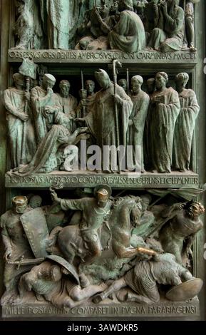 Détail du panneau de bronze de la porte d'entrée gauche au Duomo di Milano représentant des scènes avec des figures en relief et des inscriptions latines. « OBSESSIS OBSIDENTES AMBROSIVS. CHORI CARMINBYS MVLCET ;' 'THEODOSIVS AMBROSIO CORAM SVBMISSE SE GERUNS ET CLEMENTER' ET 'MILLE POST ANNIS COMPARET IN PVGNA PARABIAGENSI.' Cette scène représente probablement un événement historique ou religieux impliquant un membre Ambrose, une figure importante de l'histoire de Milan. Les portes en bronze de la cathédrale de Milan sont connues pour leurs détails complexes et leurs représentations d'événements historiques et religieux. Milan, Italie. Banque D'Images