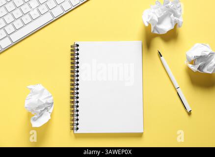 Ouvrez le carnet vierge, le papier froissé, le stylo et le clavier de l'ordinateur sur fond jaune, plat Banque D'Images