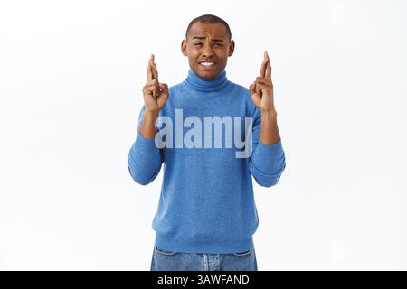 Portrait de jeune homme afro-américain plein d'espoir croisez les doigts bonne chance, frognant et calmant inquiets, en attendant des résultats importants, priant pour le rêve Banque D'Images