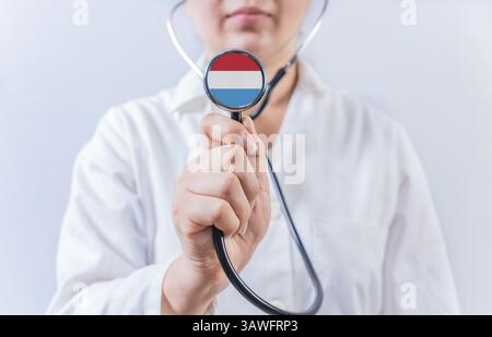 Médecin féminin tenant un stéthoscope avec drapeau luxembourgeois. Le système national de santé luxembourgeois Banque D'Images