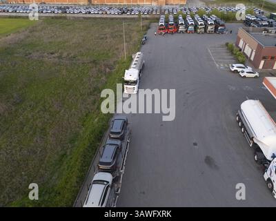 Olza, Italie 1er avril 2025 paysage logistique aérien, semi-camions, transporteurs de voitures naviguant dans le parking bondé avec l'inventaire automobile stationné ne Banque D'Images