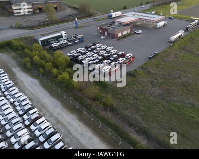 Olza, Italie 1er avril 2025 vue aérienne d'un centre logistique automobile gérant l'importation, le dépôt et les droits de douane avec des camions déchargeant des véhicules et de grands p Banque D'Images