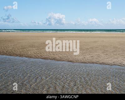 Les vagues tapent doucement contre le rivage à Inchydoney Beach, où le sable doux s'étend sous un ciel bleu clair. La lumière du soleil améliore l'atmosphère sereine pour Banque D'Images
