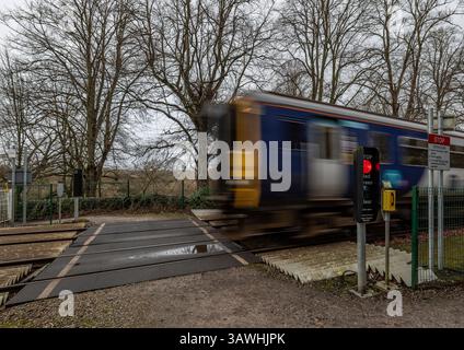 Passage à niveau de chemin de fer pour piétons avec feux de circulation dans un environnement rural avec feu rouge montrant et train à vitesse floue approchant. Banque D'Images