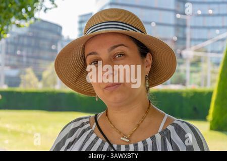 Portrait d'une femme de 40-45 ans en plein air par une journée ensoleillée. Une femme dans un chapeau de paille et un chemisier rayé sur le fond d'un ci moderne Banque D'Images