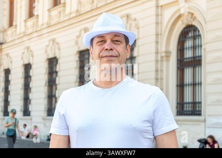 Un homme de 50-55 ans dans un élégant chapeau blanc se dresse sur le fond d'un bâtiment européen classique Banque D'Images