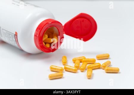 Pilules de médecine jaune renversant hors de bouteille blanche isolé sur fond Banque D'Images